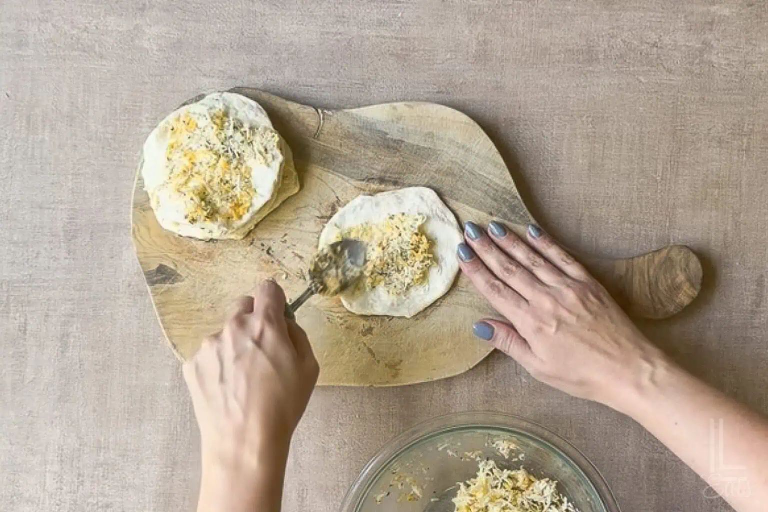 Spreading cheesy butter mixture over flattened biscuit dough.