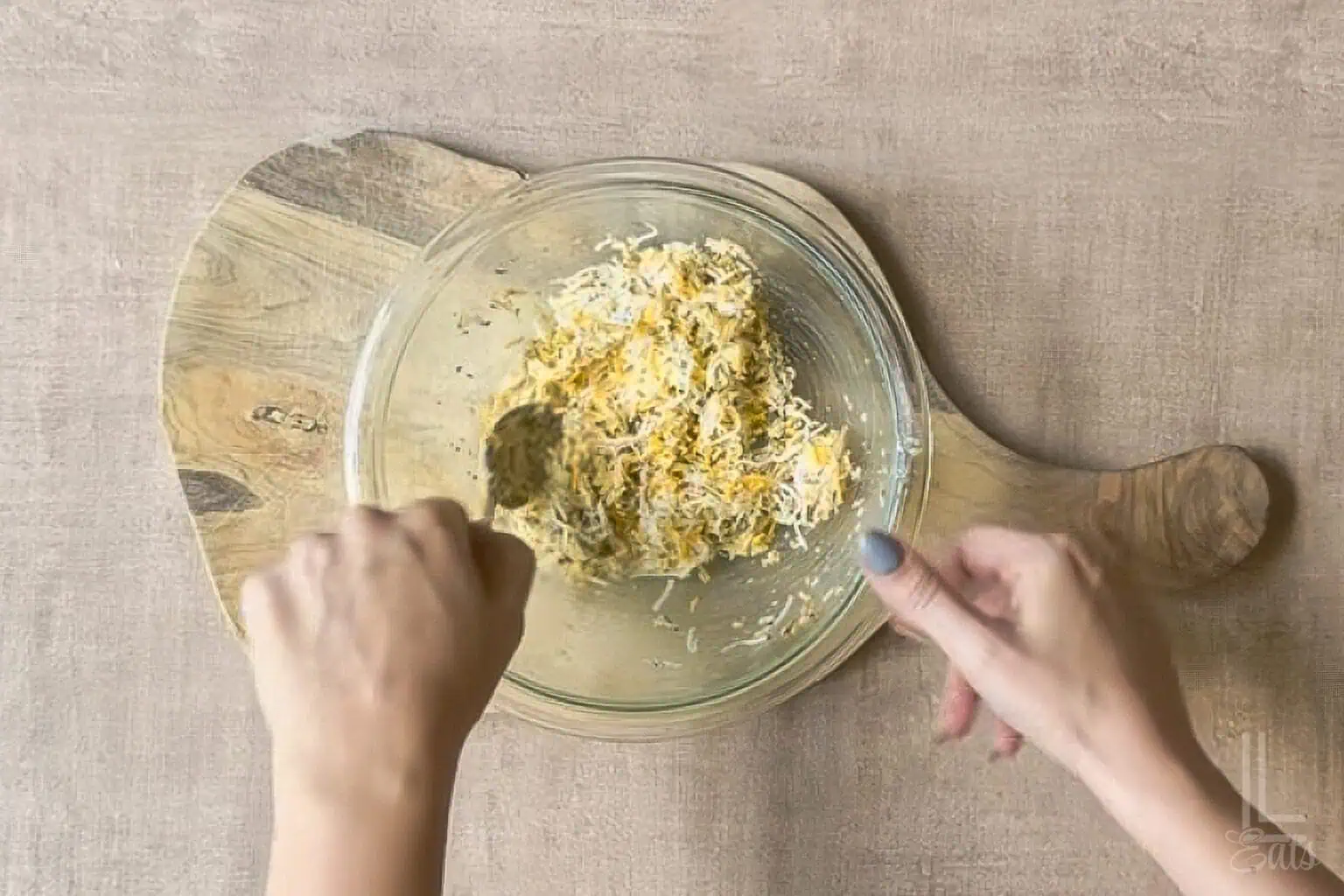 Mixing shredded cheese and garlic in a glass bowl for cheesy garlic pull apart bread.
