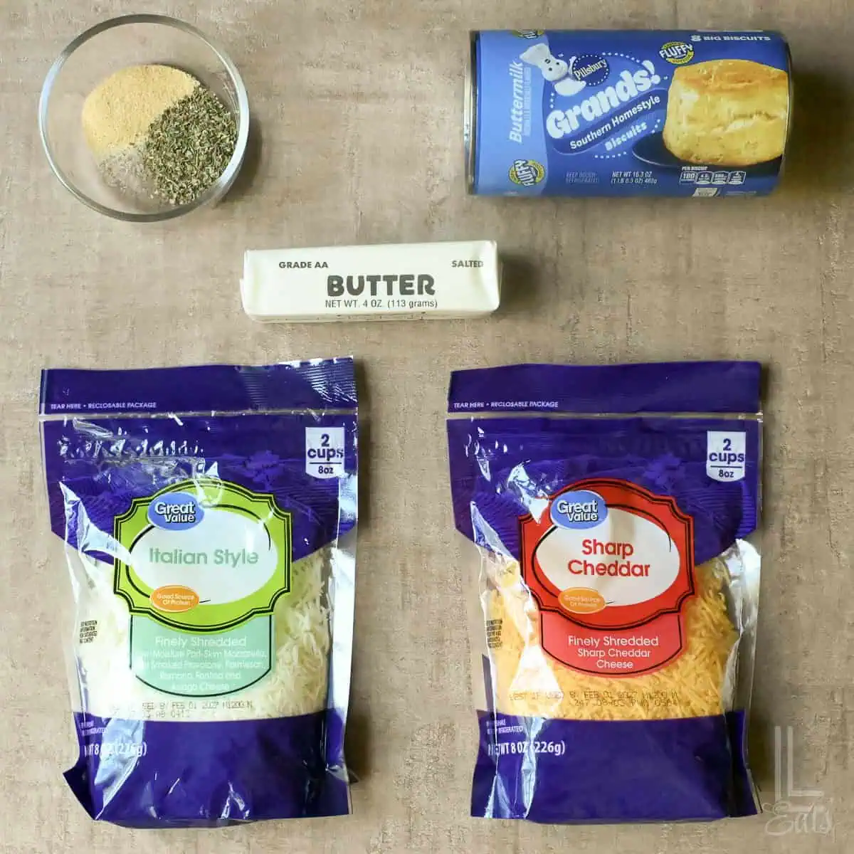 Ingredients for cheesy garlic pull apart bread with butter, shredded cheese, herbs, and seasonings.