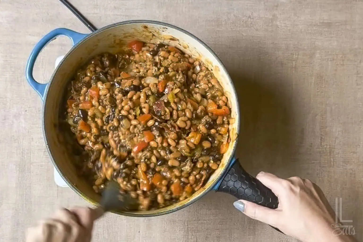 Hearty cowboy baked beans with ground meat and vegetables stirred in a pot.