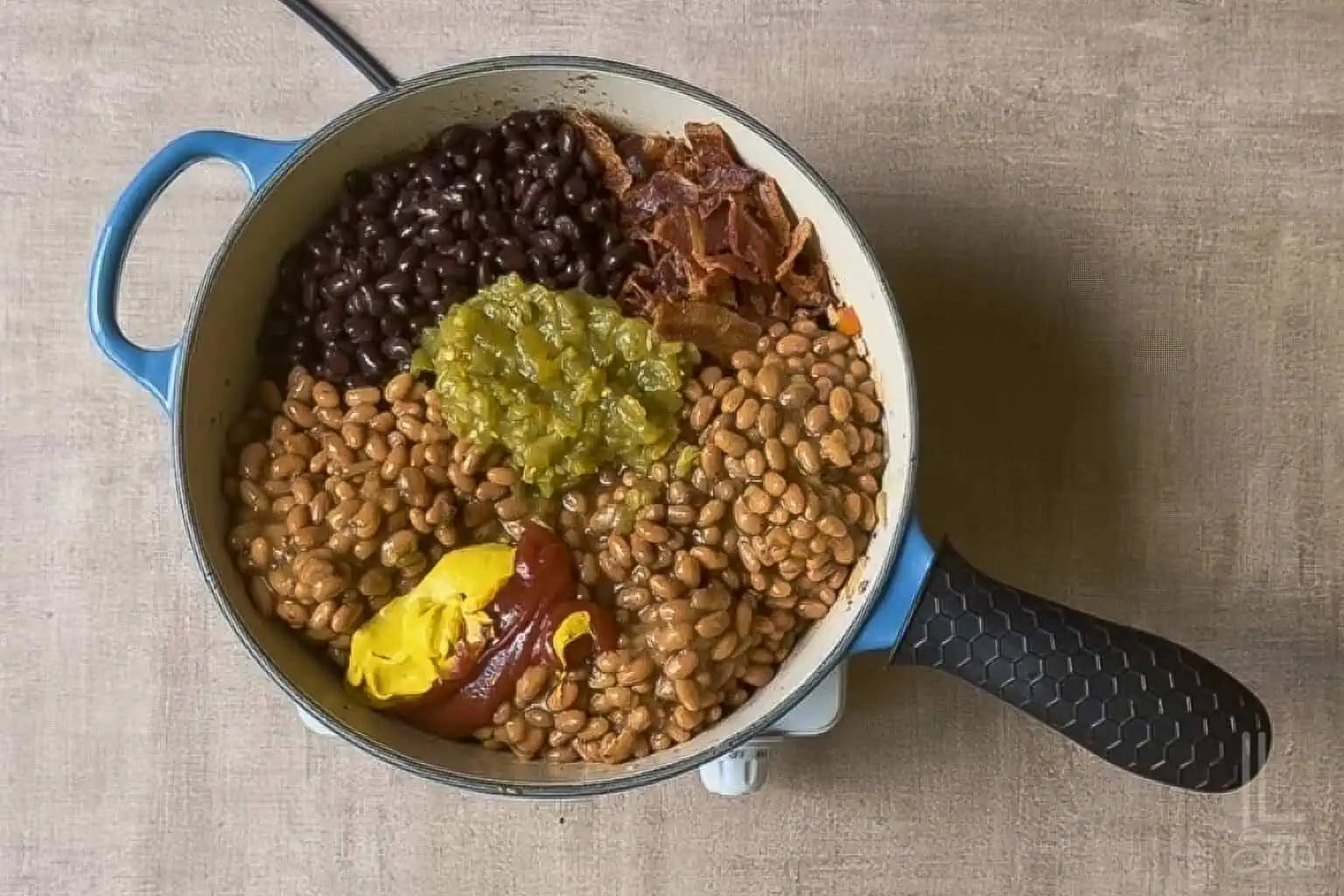 Assorted baked beans and ingredients in a pot for Cowboy Baked Beans recipe.