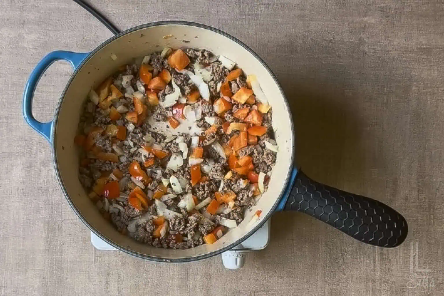 Cooking ground beef with diced peppers and onions in a blue pot for Cowboy Baked Beans.
