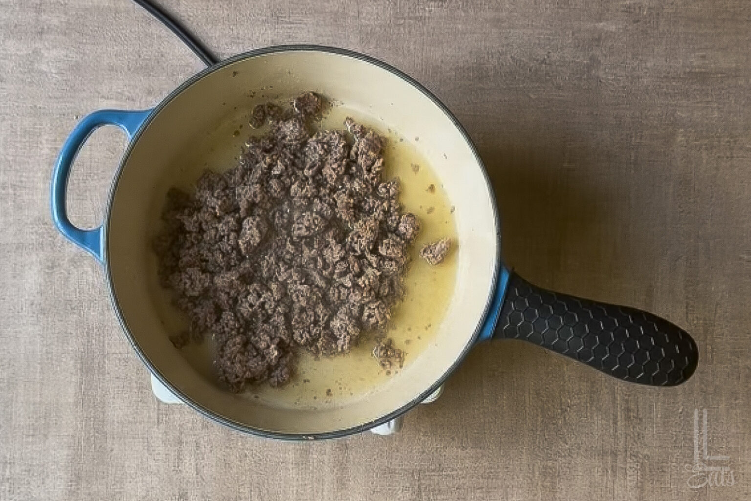 Cooking ground beef in a blue skillet for baked beans recipe.