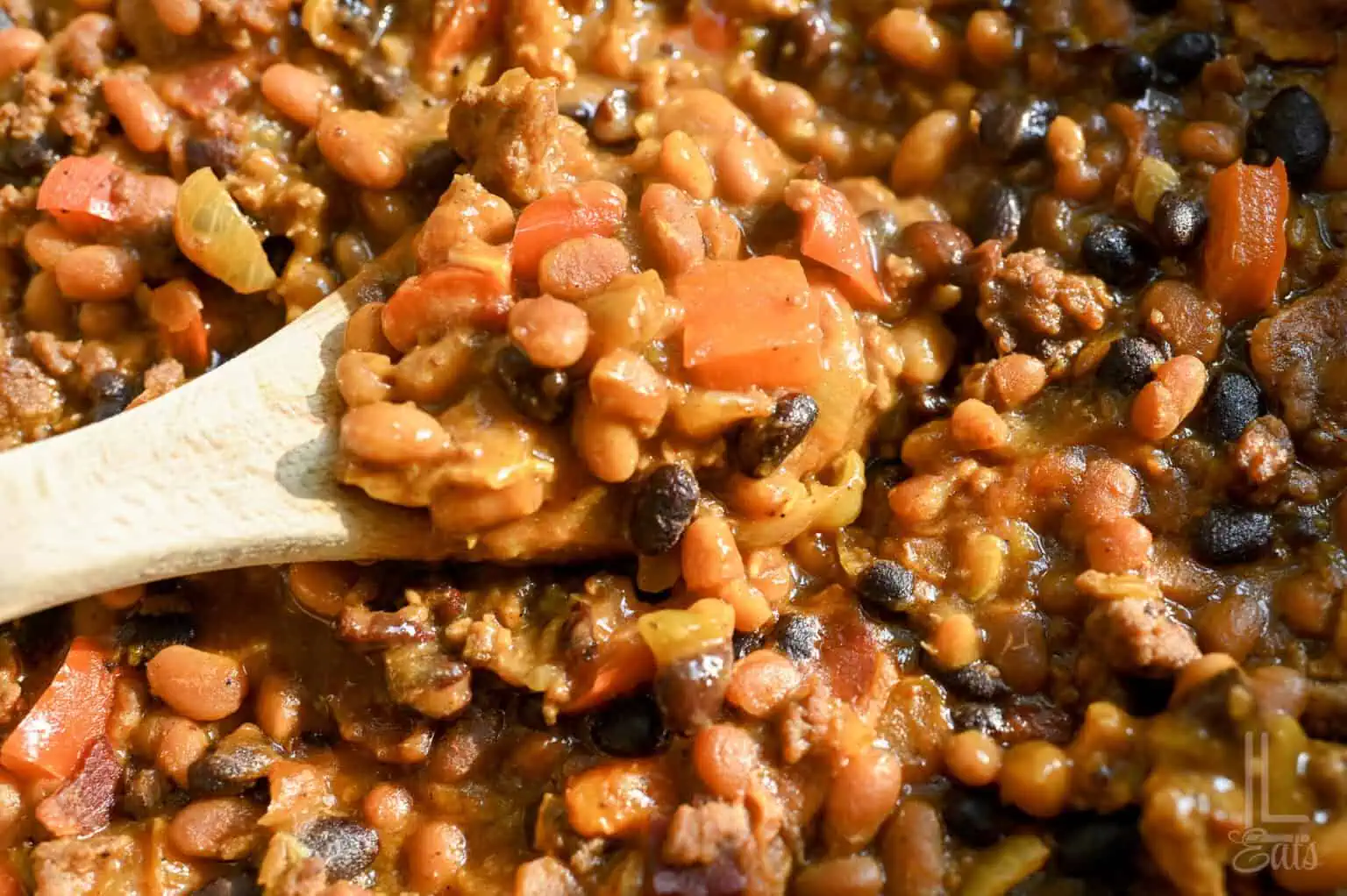 Close-up of hearty cowboy baked beans with ground meat and vegetables in a spoon.