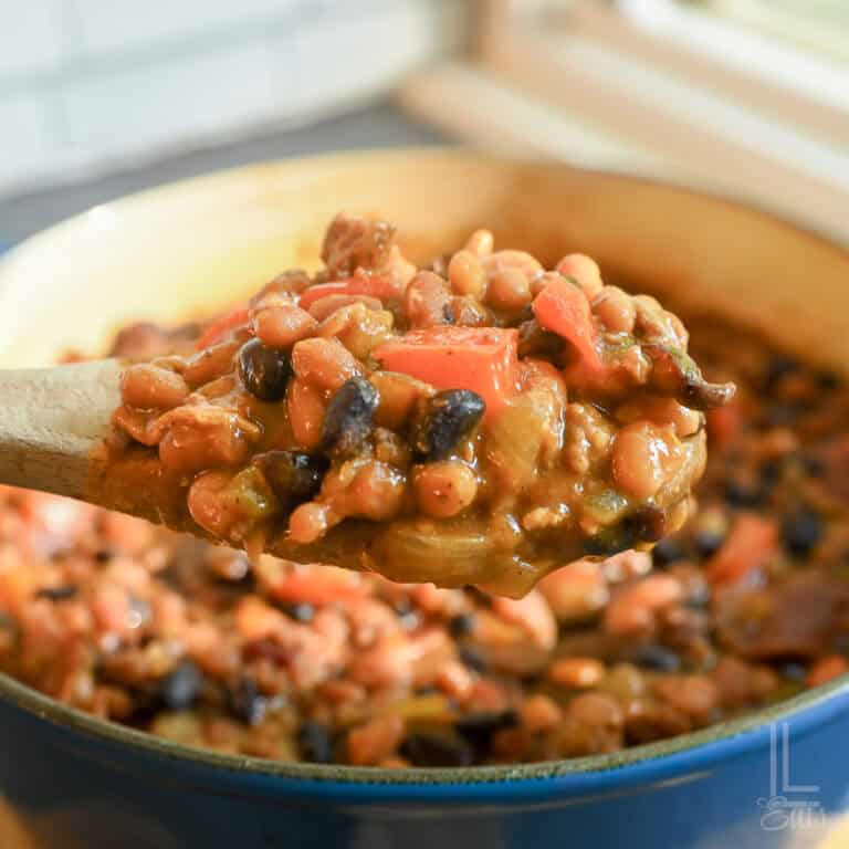 wooden spoon filled with cowboy baked beans in front of a cooking dish.