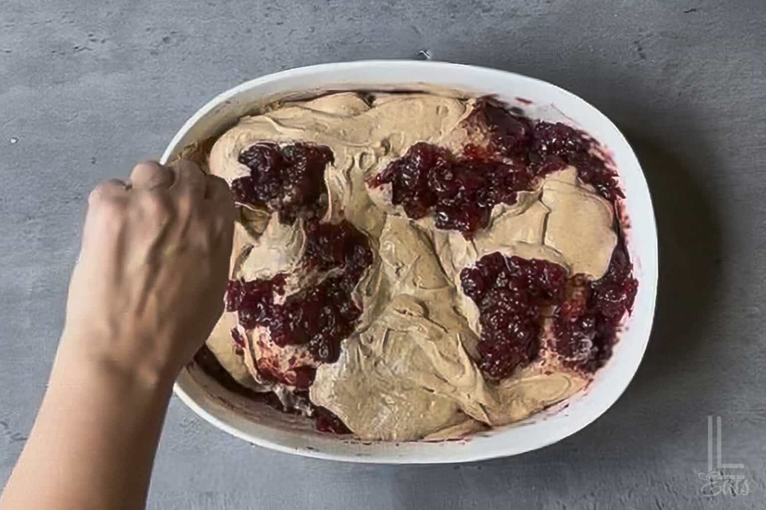 Stirring cranberry mixture and cake batter in a baking dish.