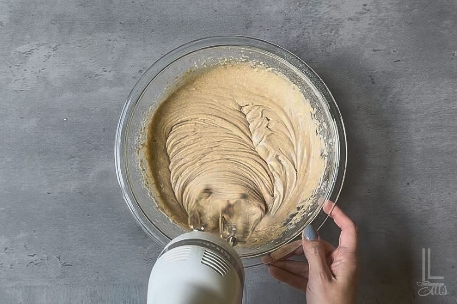 Mixing spice cake batter in a glass bowl with a hand mixer for cranberry cobbler.