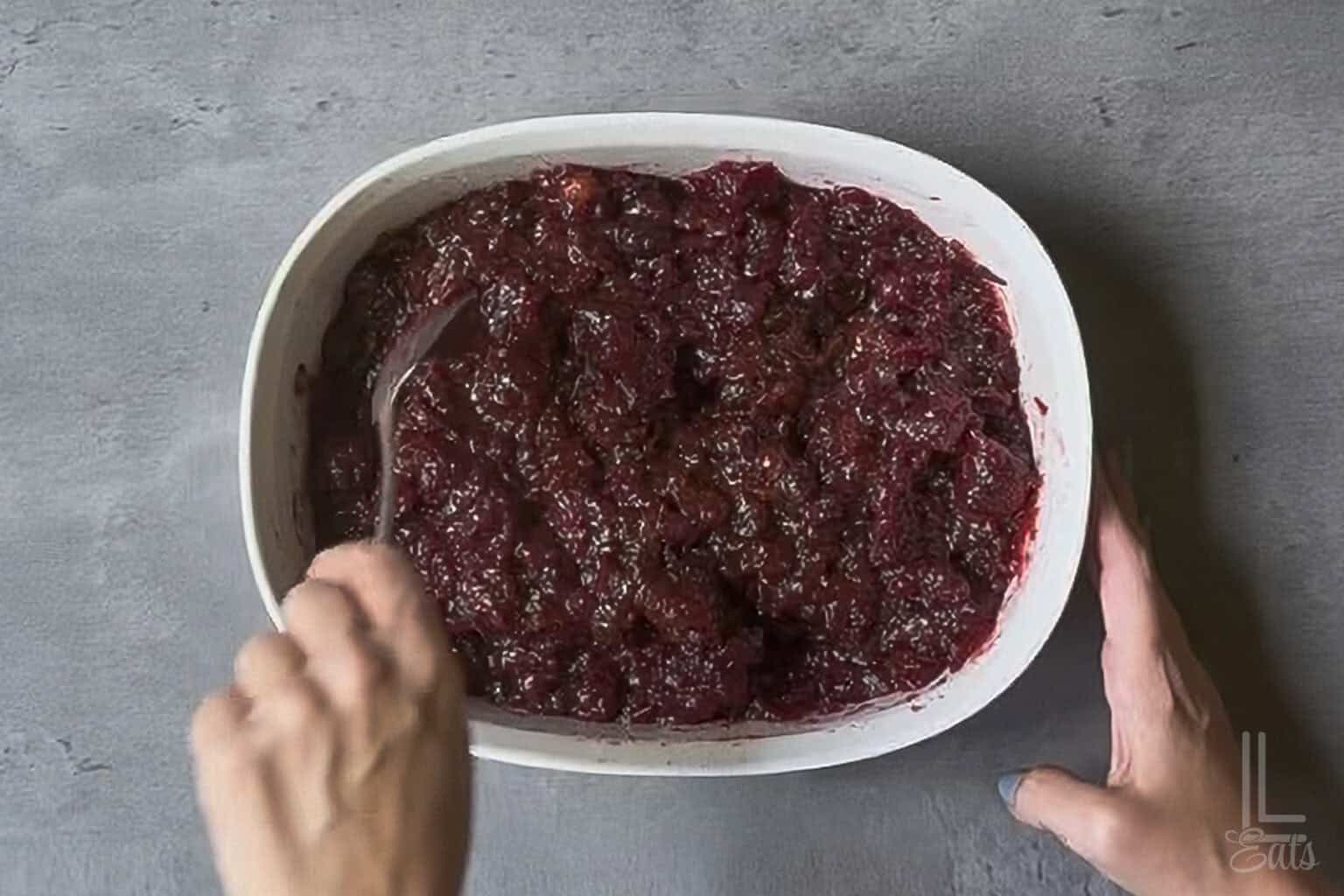 Stirring sugar and cranberry sauce in a baking dish.