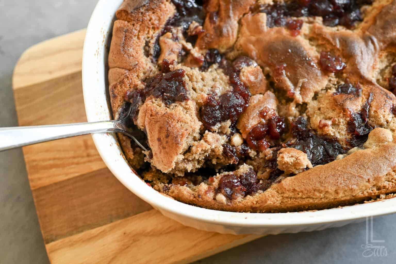 Close-up of a freshly baked cranberry cobbler in a white dish on a wooden board.