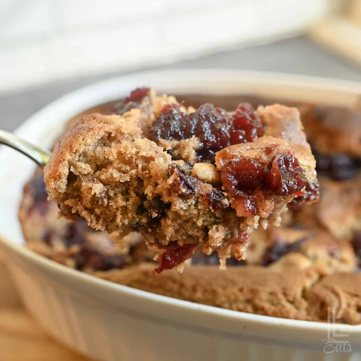 holding a large spoonful of cranberry cobbler, with spice cake and cranberry sauce.