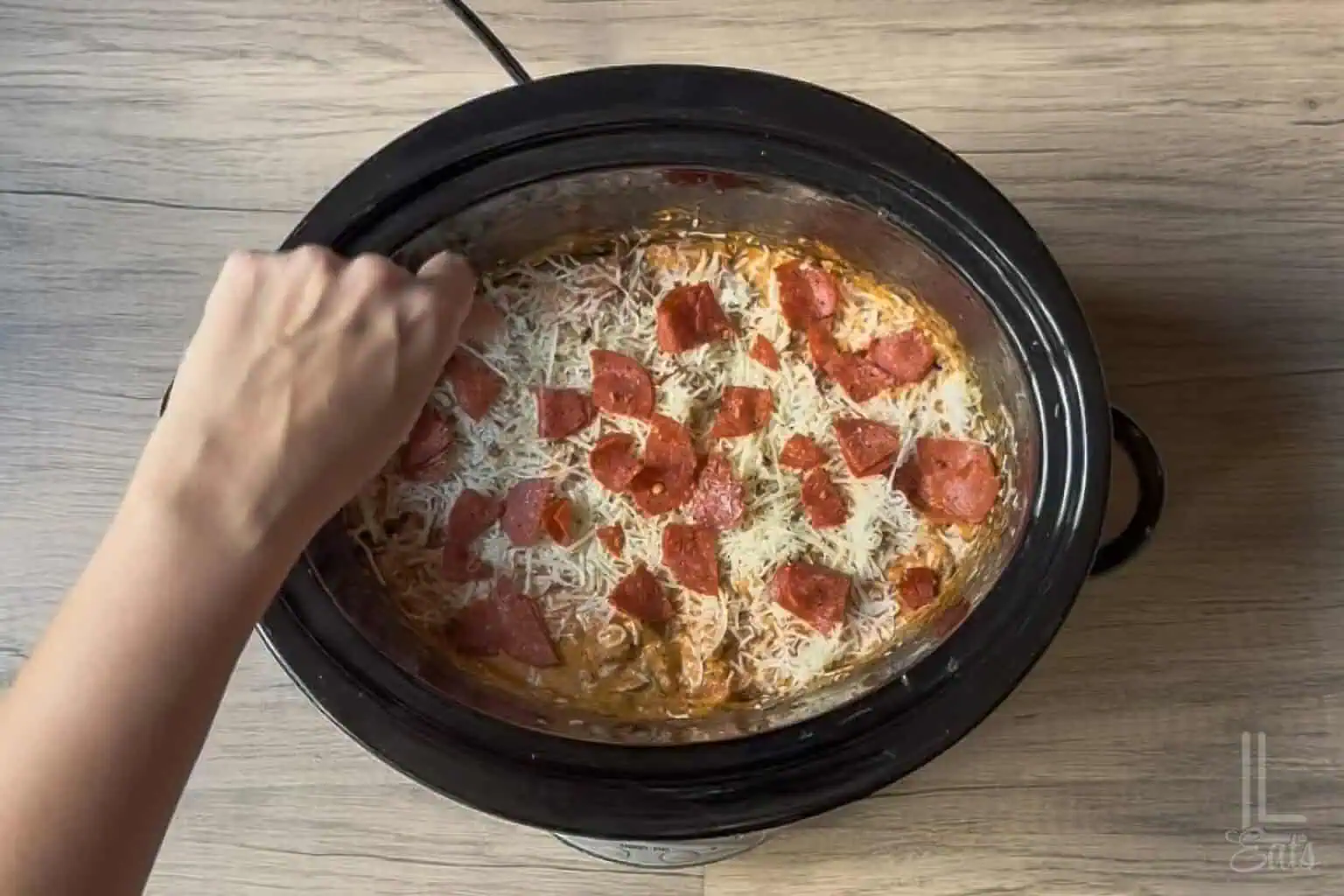 Sprinkling the finished pizza dip with shredded cheese and leftover pepperoni.
