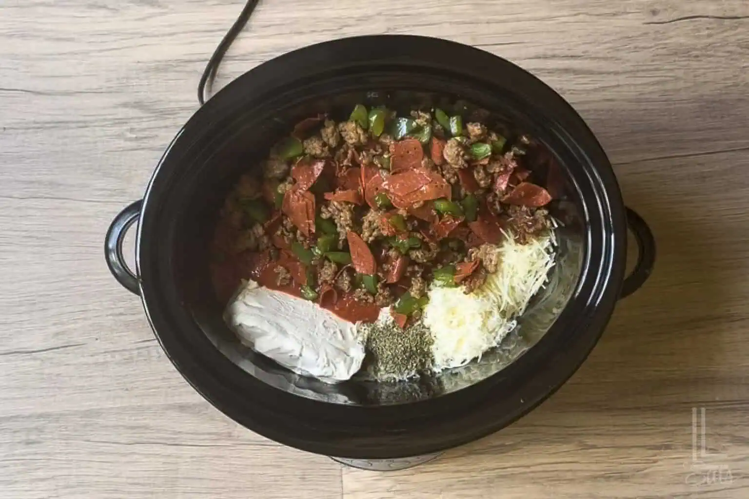 Ingredients for Crock pot pizza dip in a slow cooker, including sausage mixture, pepperoni, cream cheese, shredded cheese, and pizza sauce.