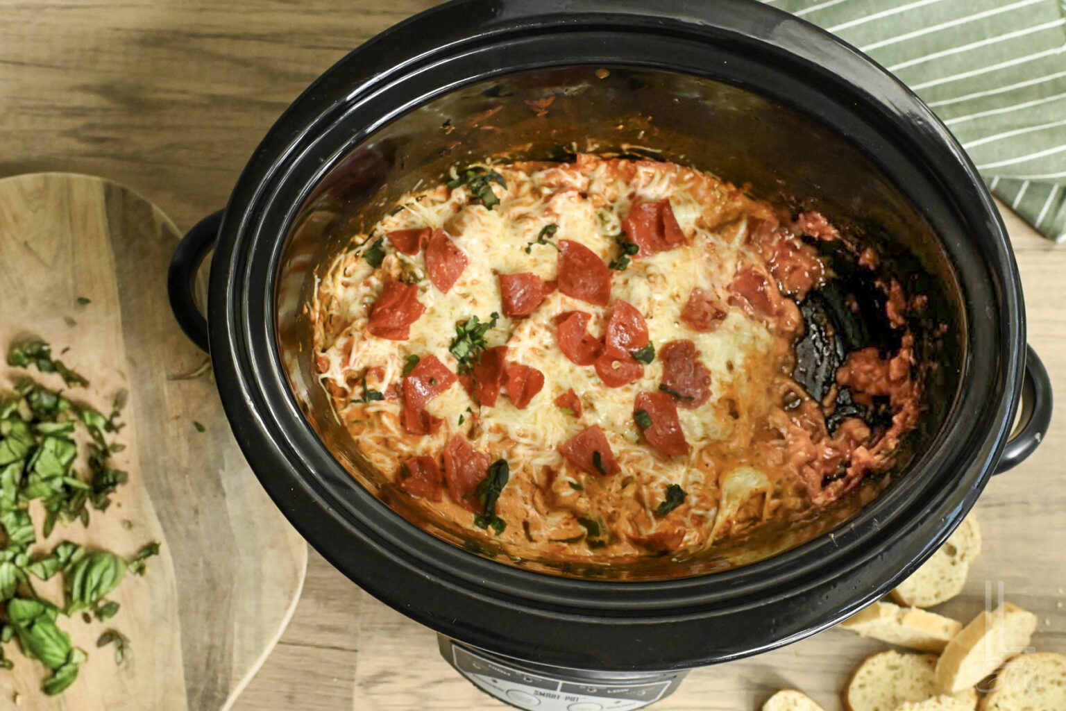 Crock Pot Pizza Dip with cheese, pepperoni, and basil in a slow cooker.