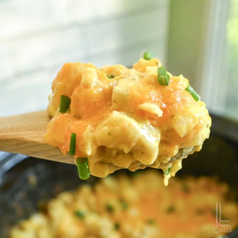 holding a spoonful of cheesy potatoes in front of a crock pot.