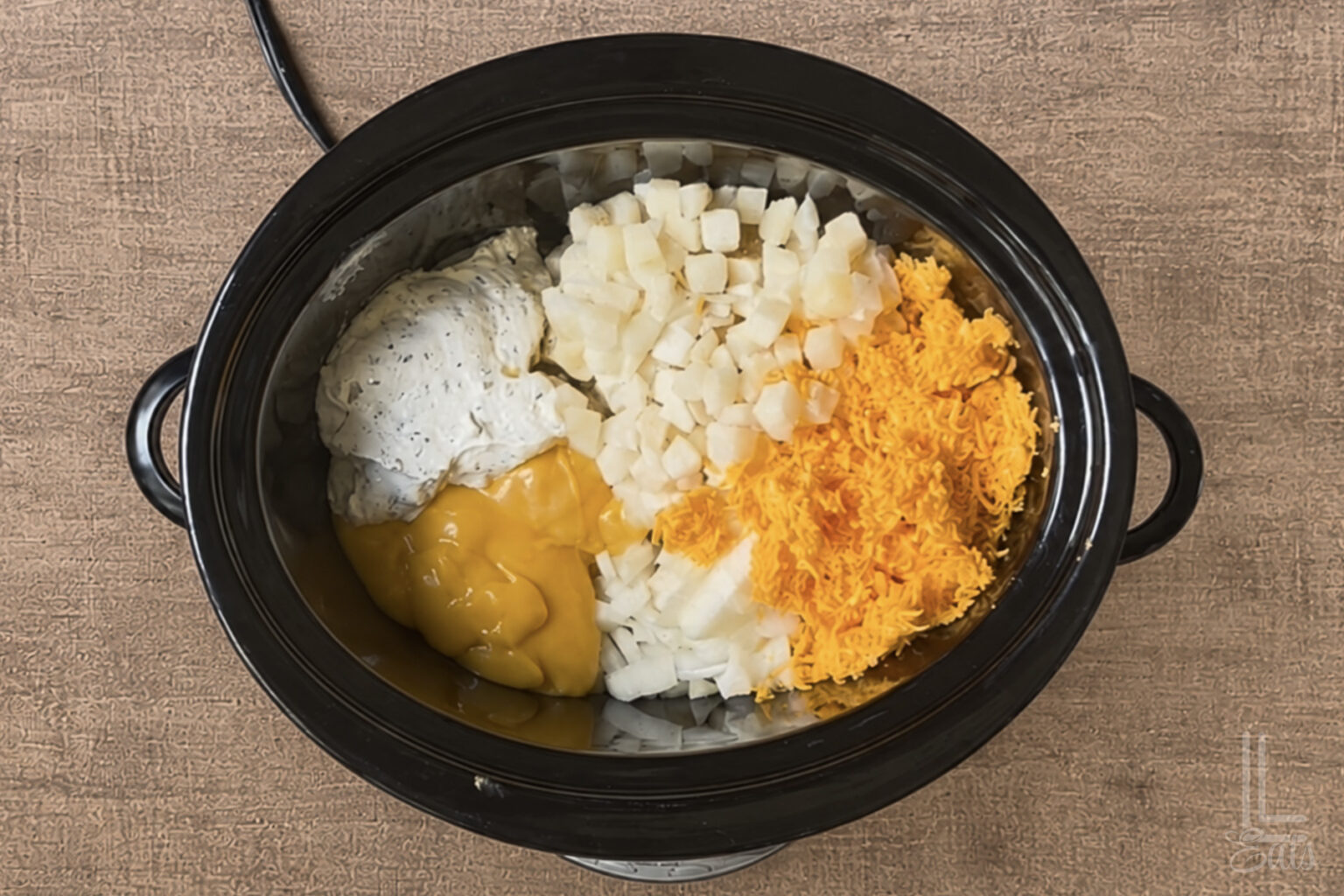 Combined ingredients (hash browns, cheddar cheese soup, shredded cheese, French onion dip, etc.) in a Crock Pot.