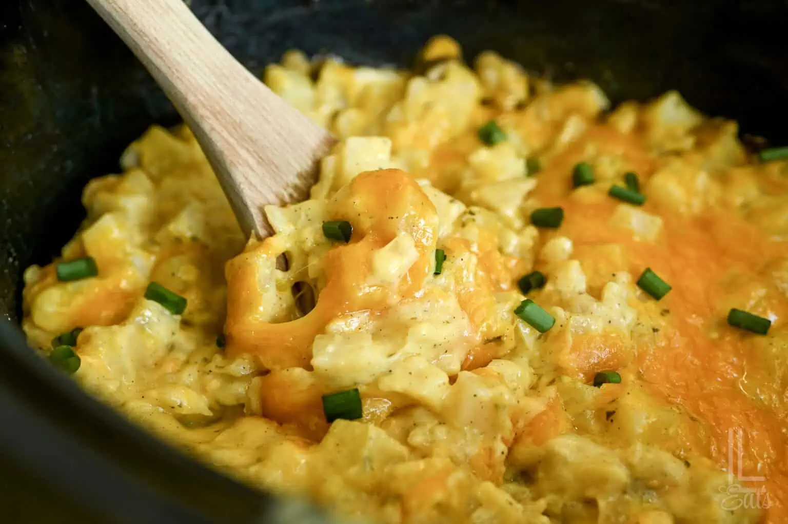 Creamy cheesy potatoes with green onions in a crockpot, ready to serve.