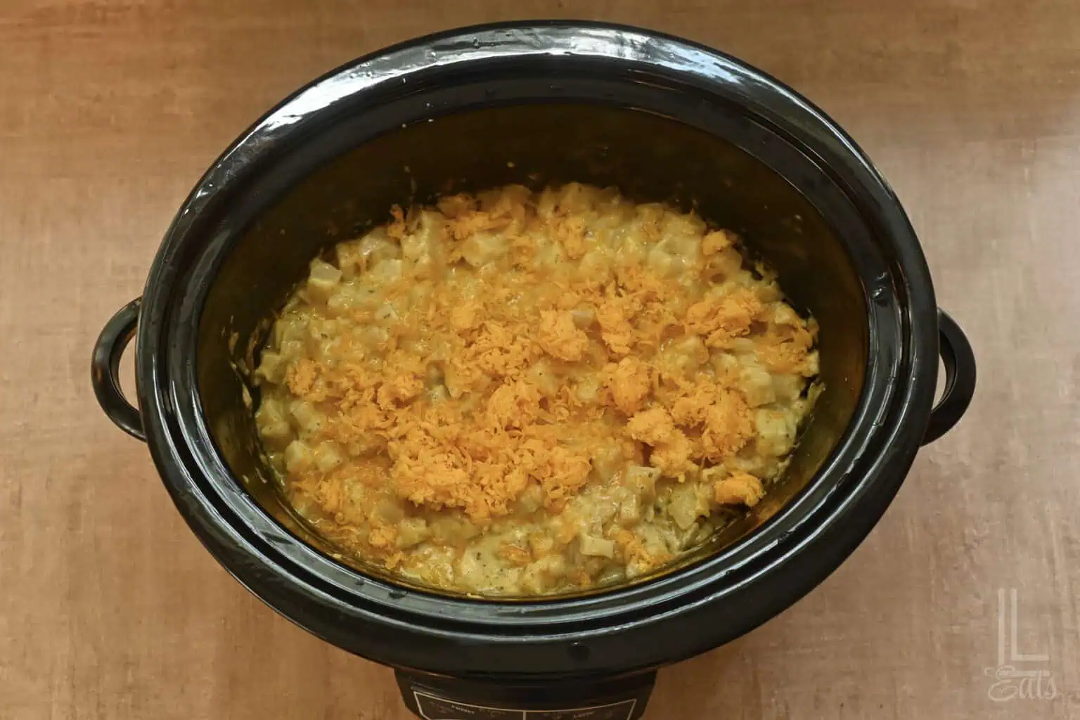 Crockpot cheesy potatoes topped with shredded cheese and crispy topping.