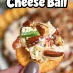 Close-up of pineapple cheese ball with bacon on a cracker, held by a hand.