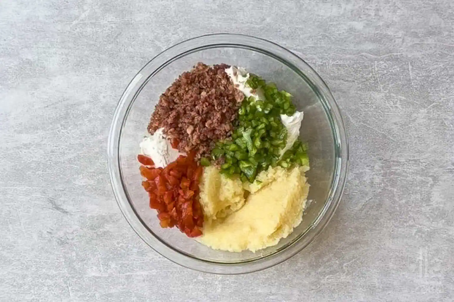 Ingredients for Pineapple Cheese Ball with Bacon in a glass bowl on a gray surface.
