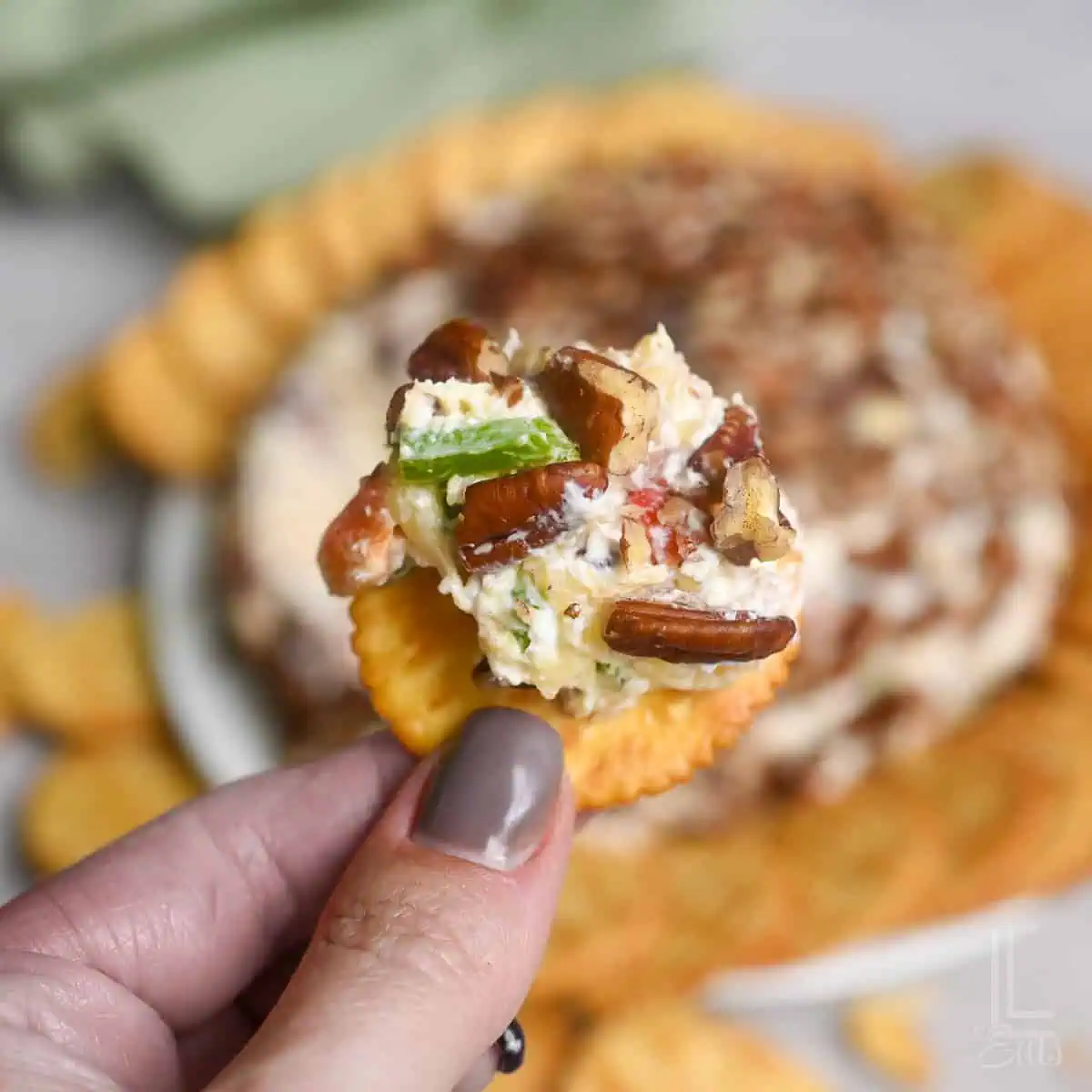 Close-up of pineapple cheese ball with bacon on a cracker, with more crackers in background.