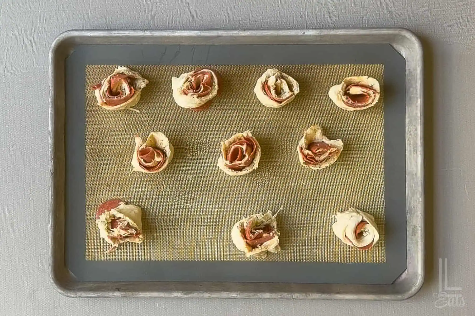 Unbaked pizza roll ups on a baking sheet ready for baking.