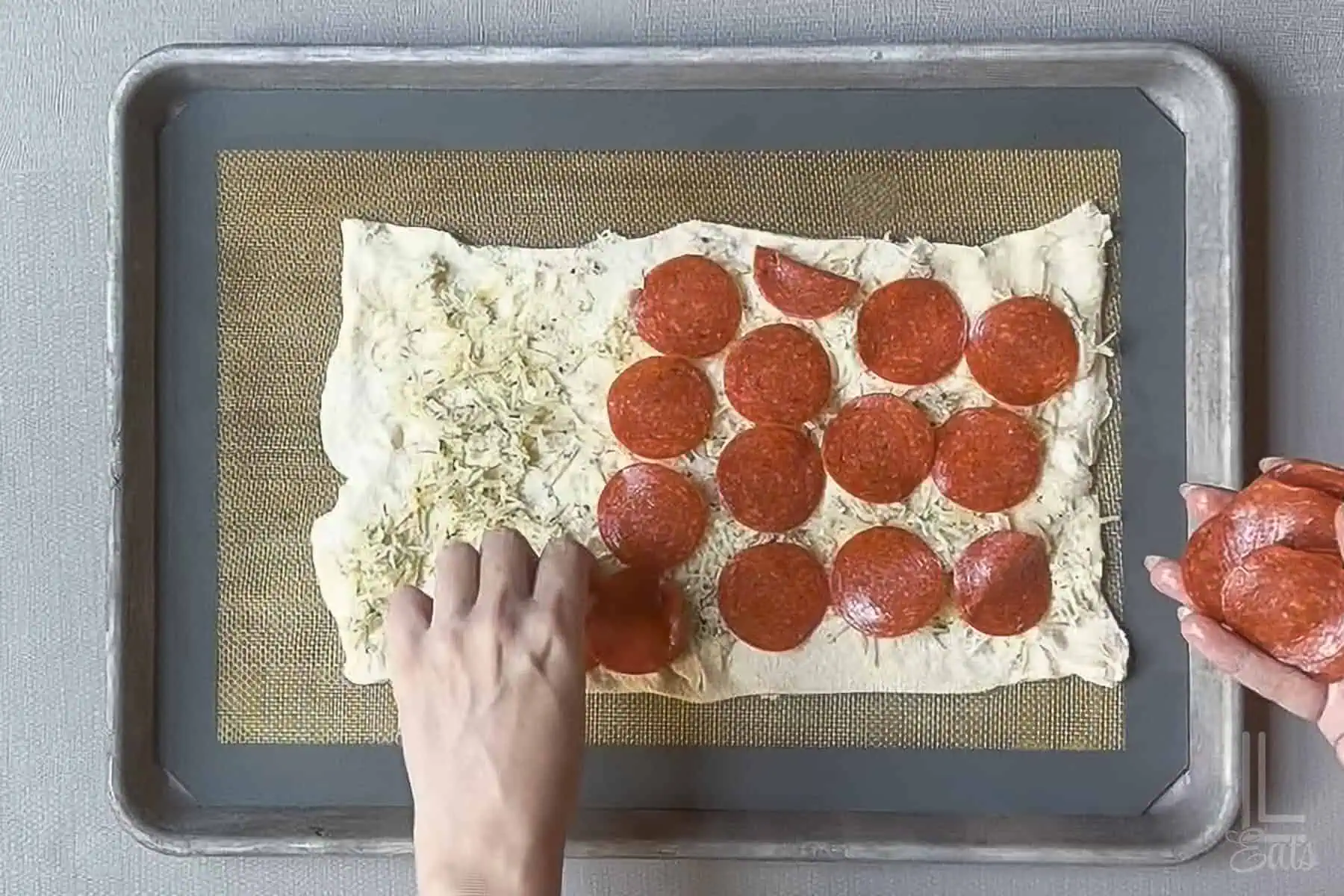 Placing pepperoni slices over the cheese and garlic filling on the crescent roll dough.