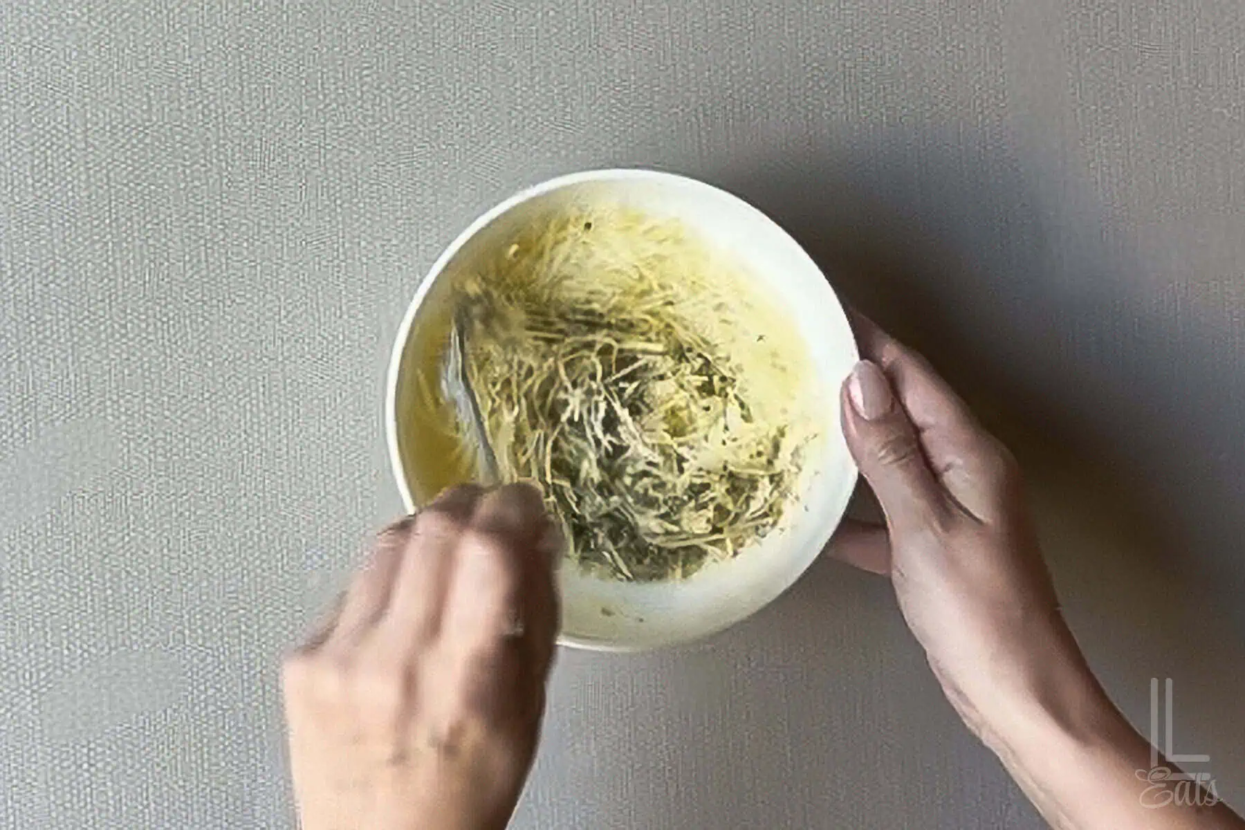 Stirring garlic butter mixture into shredded mozzarella and parmesan cheeses.