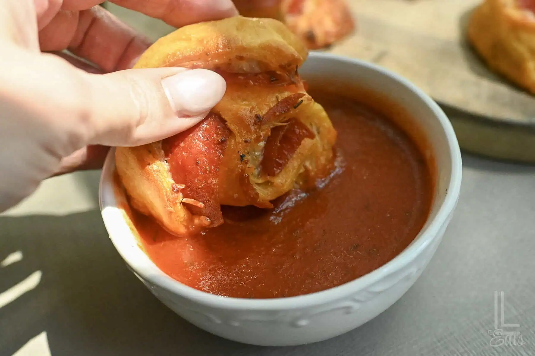 Pizza roll being dipped into pizza sauce in a white bowl.