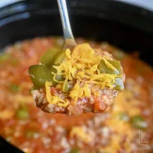 a spoonful of stuffed pepper soup, topped with shredded cheese, in front of a slow cooker.