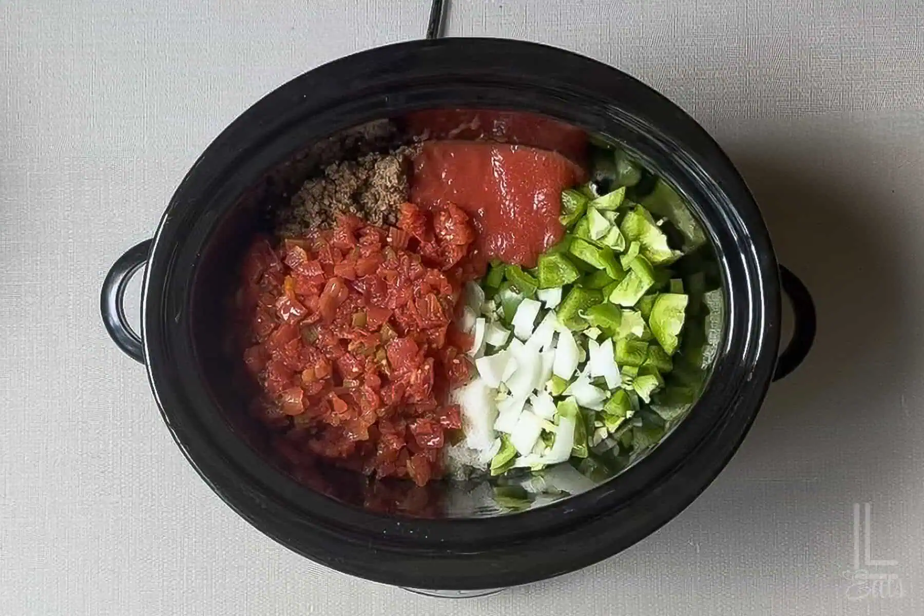 Ingredients for stuffed pepper soup in a slow cooker, including tomatoes, peppers, and ground sausage.