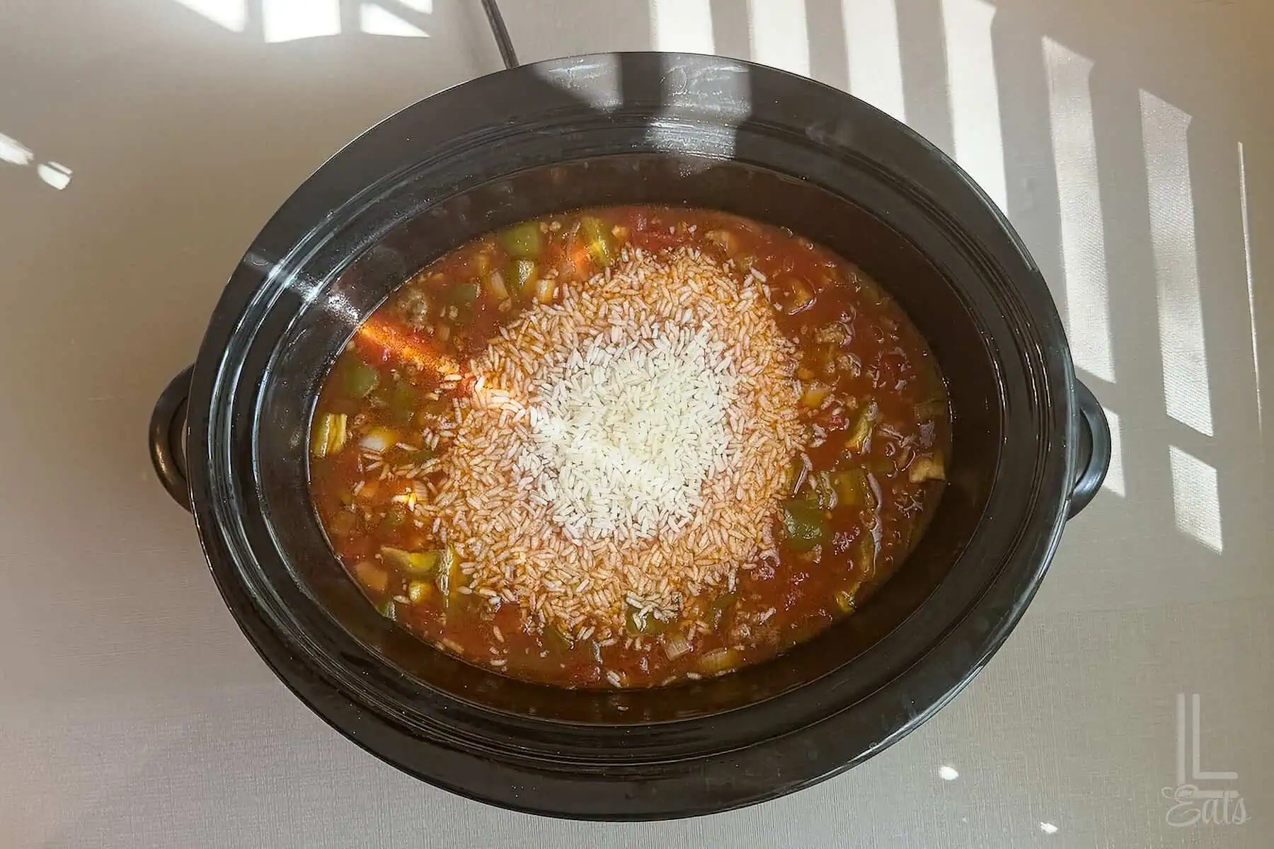 Instant rice being stirred into slow cooker stuffed pepper soup.